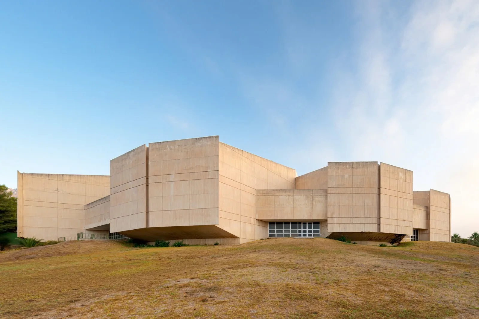 The Palacio de Congresos Torremolinos from outside — a sculptural sand-coloured concrete building on a low grassy rise.